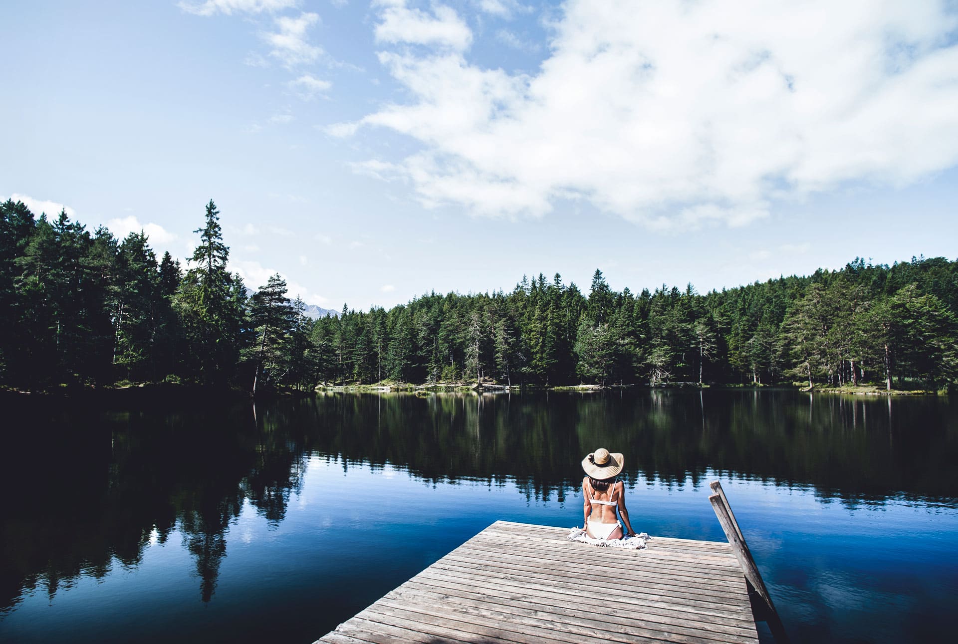 dasMAX, a lady sits on the jetty of a lake